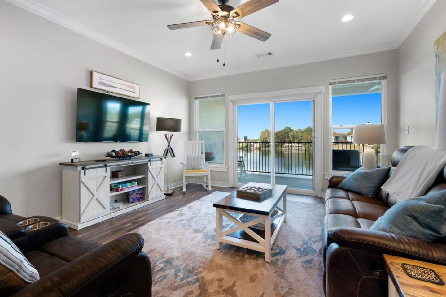 A living room with a couch , chair , coffee table , television and ceiling fan.