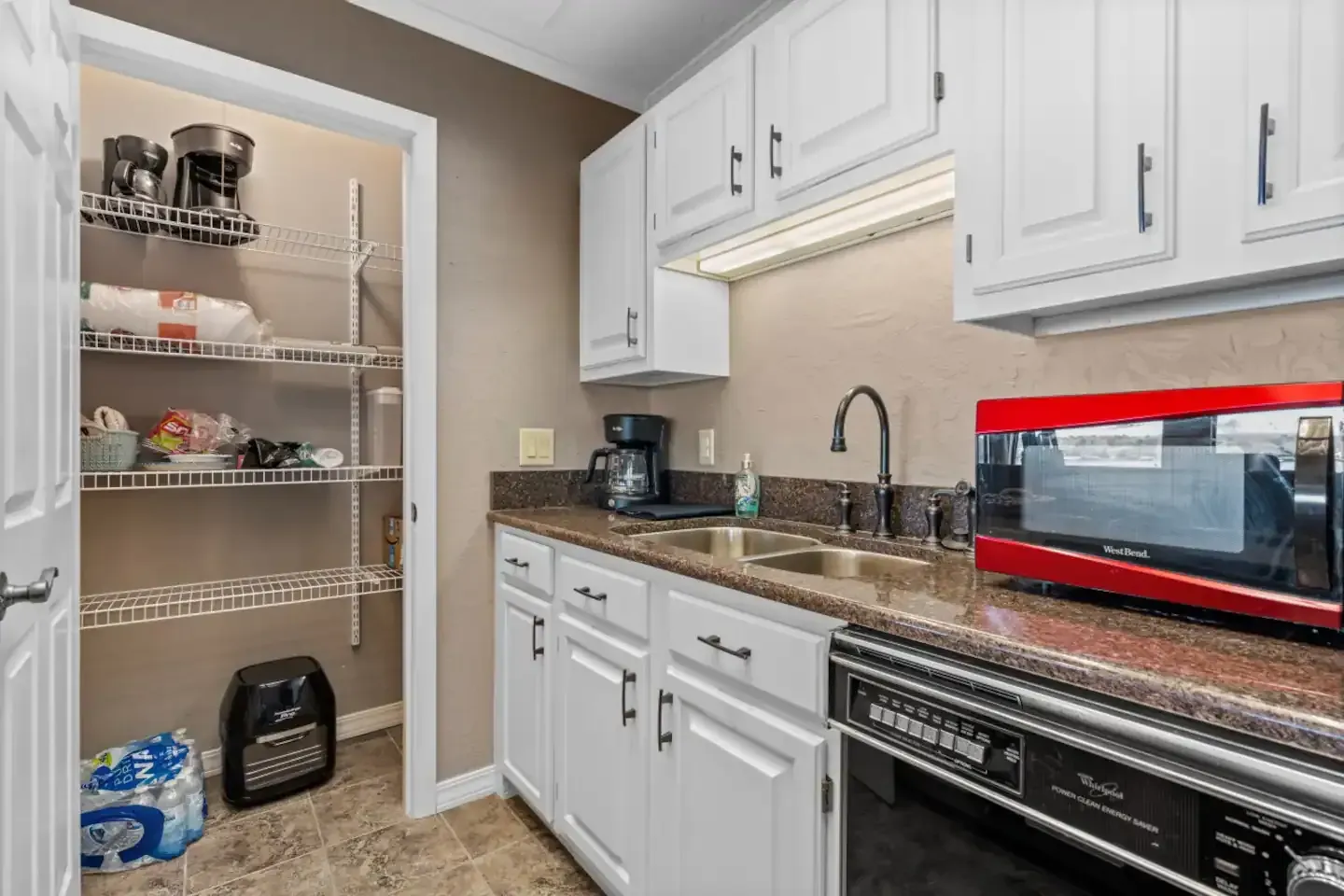 A kitchen with white cabinets , a red toaster oven , a sink , and a pantry.
