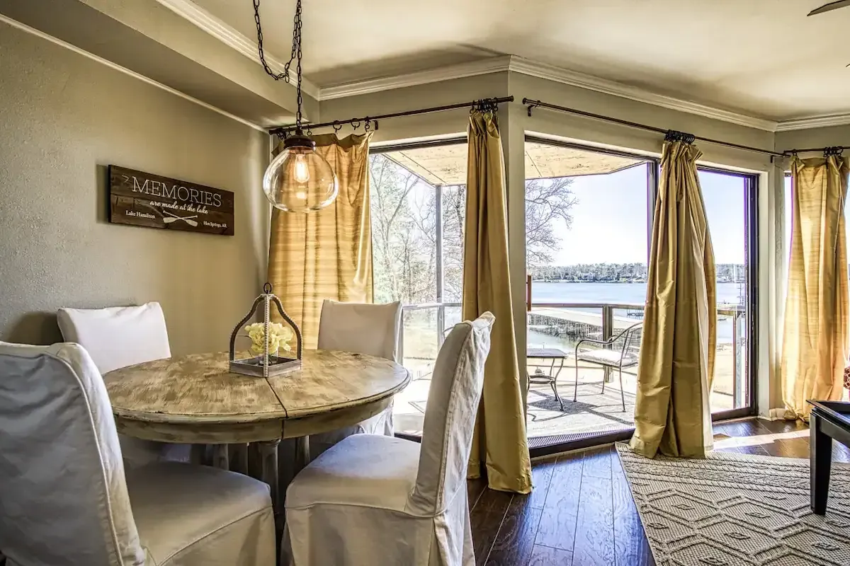 A dining room with a table and chairs and a large window overlooking a lake.