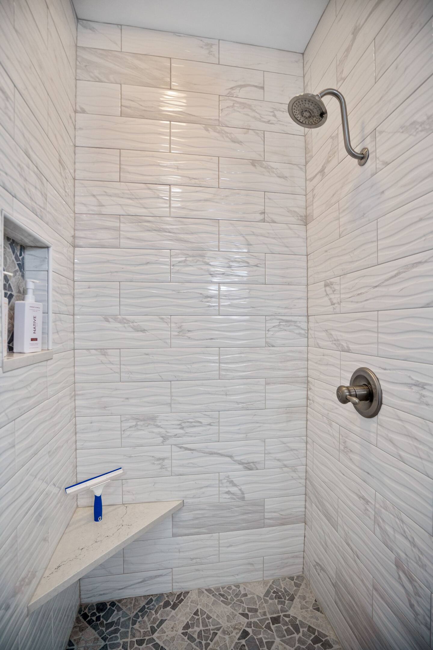 A walk in shower with a bench and a shower head.