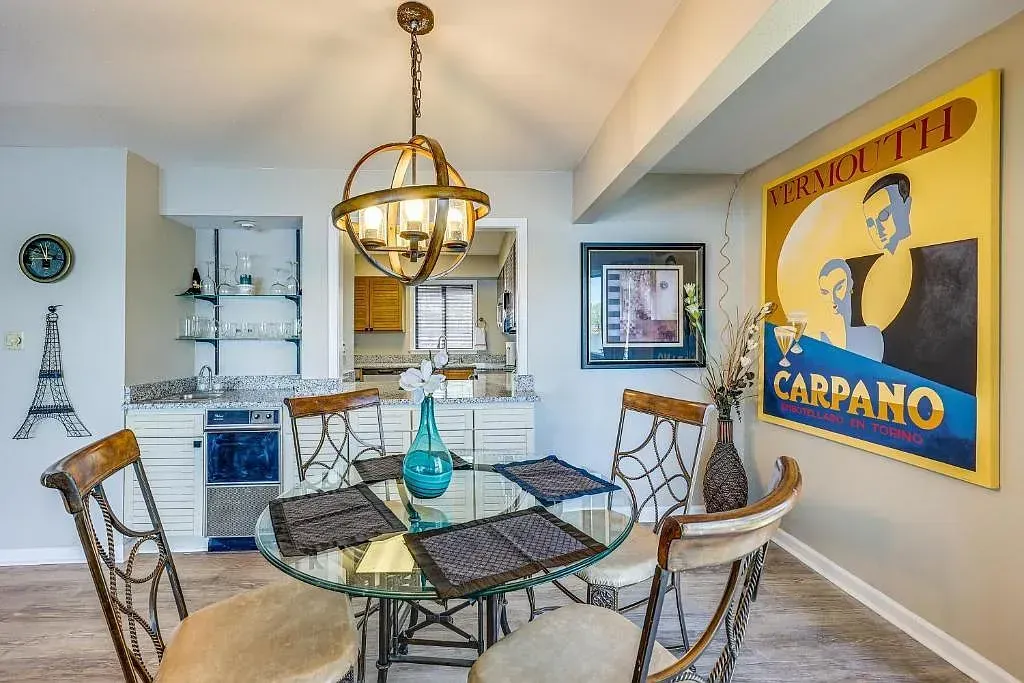 A dining room with a glass table and chairs and a painting on the wall.