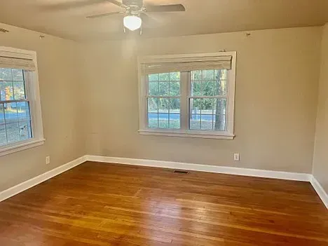 Empty bedroom with hardwood floors, two windows, and a ceiling fan.