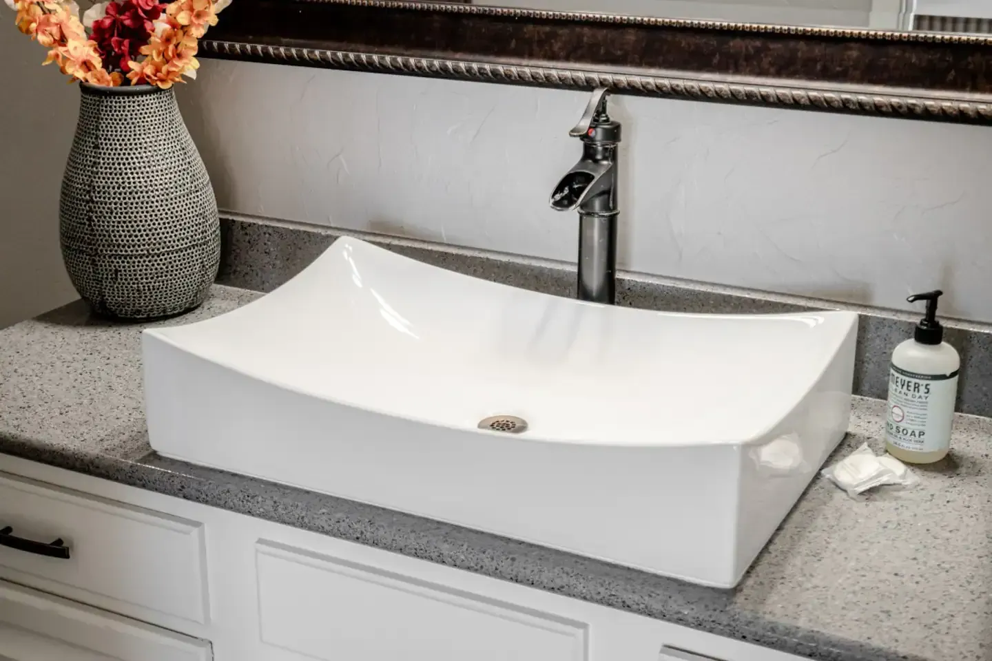 A bathroom sink with a vase of flowers on top of it.