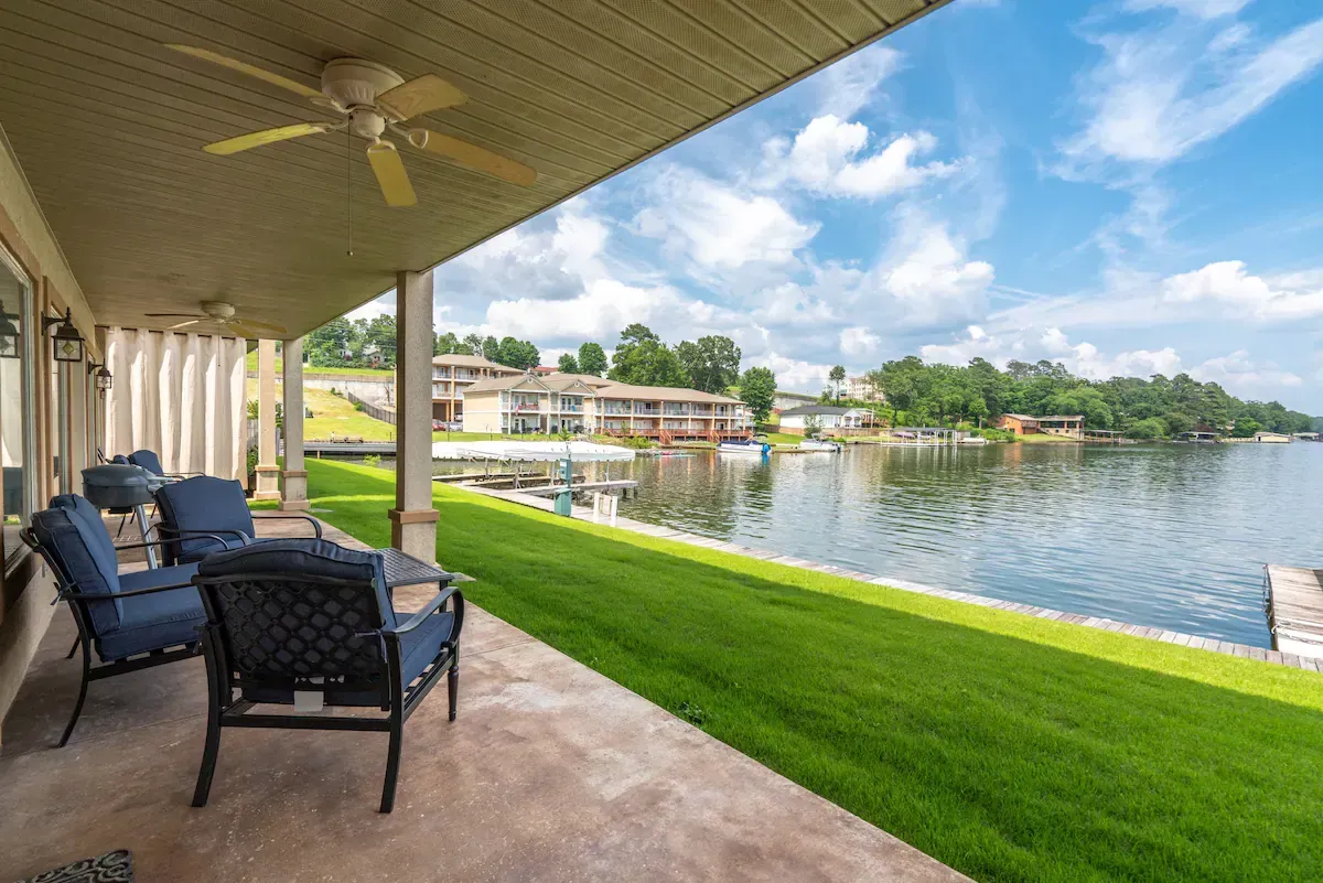 A patio with chairs and a ceiling fan overlooking a lake.