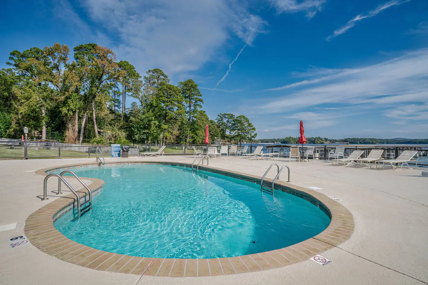 A large swimming pool surrounded by trees and chairs on a sunny day.