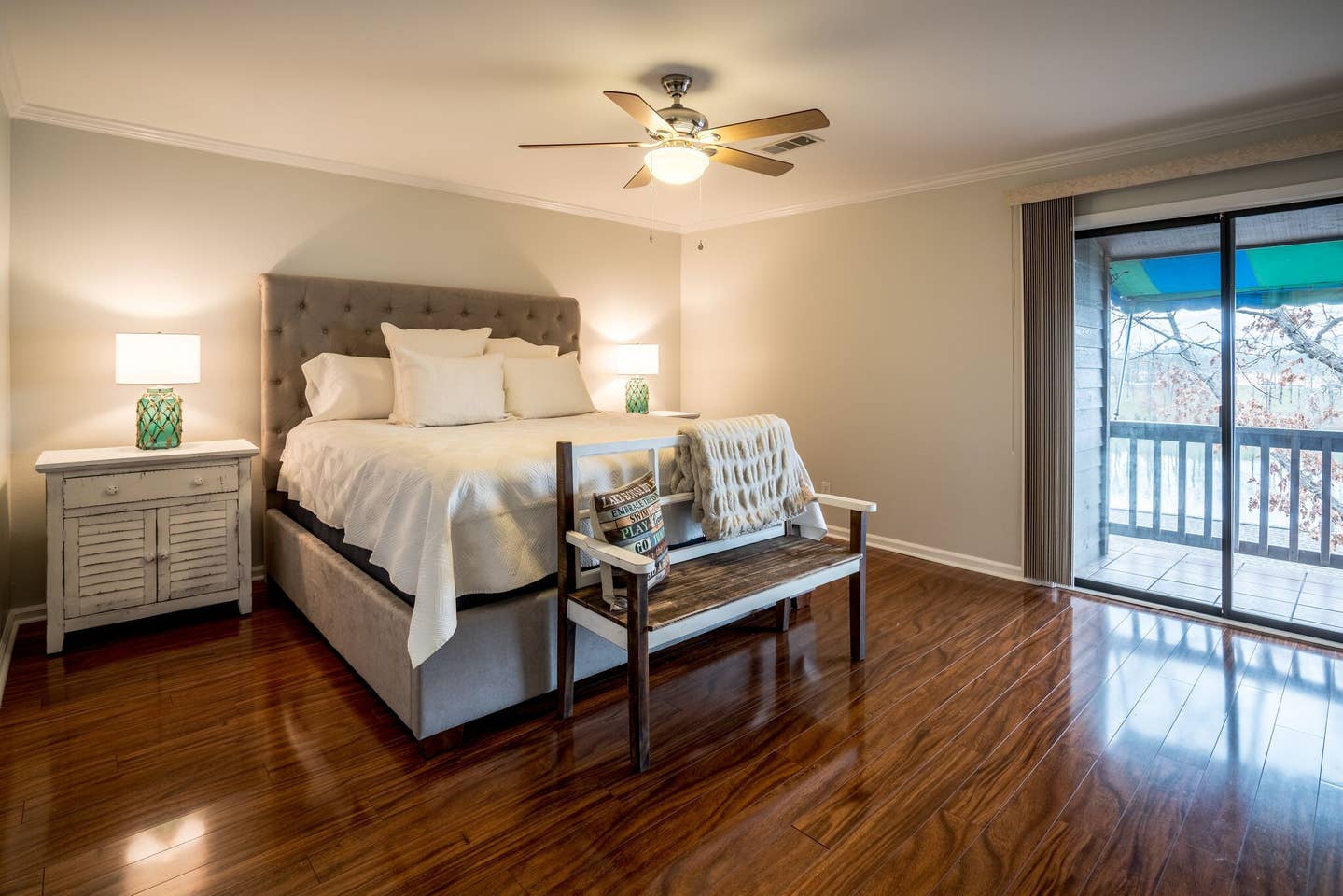 A bedroom with a king size bed , bench , nightstand and ceiling fan.