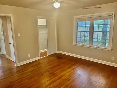 Empty room with hardwood floors, closet, window with blind, and ceiling fan. Beige walls.