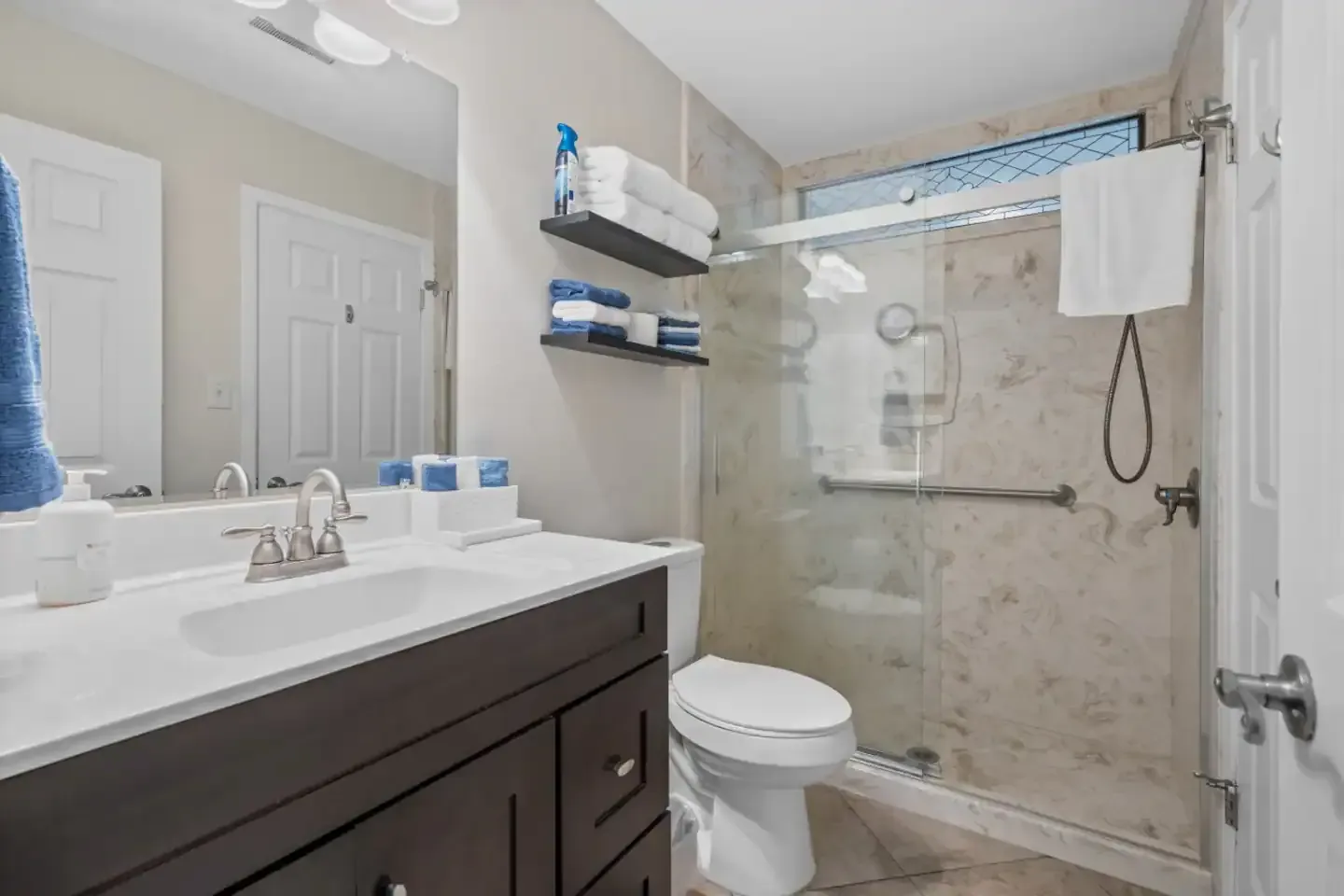 A bathroom with a toilet , sink , mirror and walk in shower.