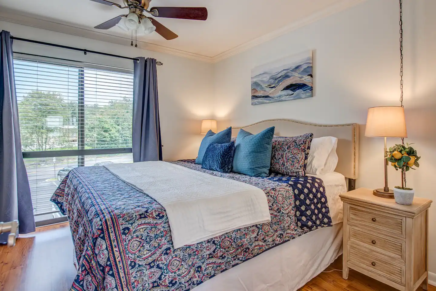 A bedroom with a king size bed , nightstand , lamps and a ceiling fan.