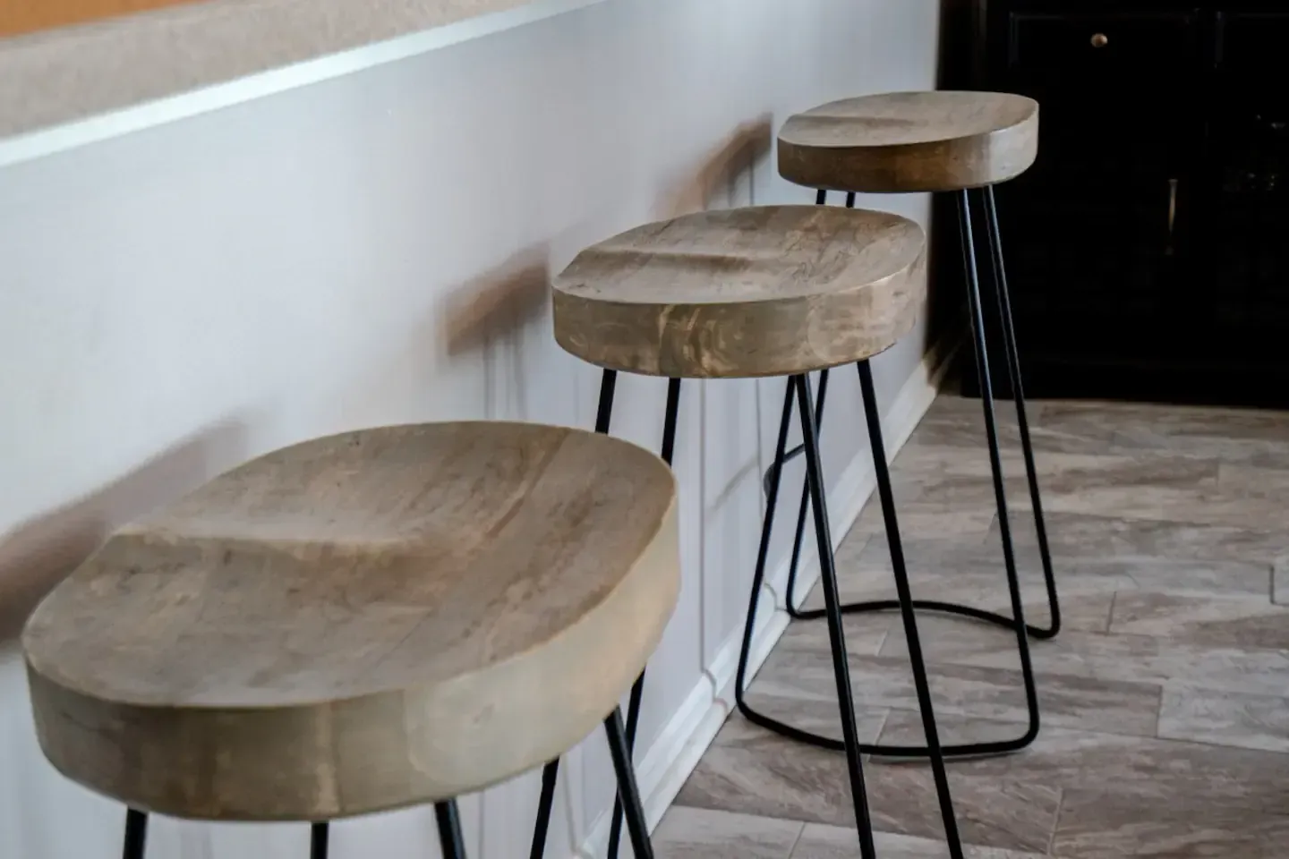 Three wooden bar stools are sitting next to each other on a tiled floor.