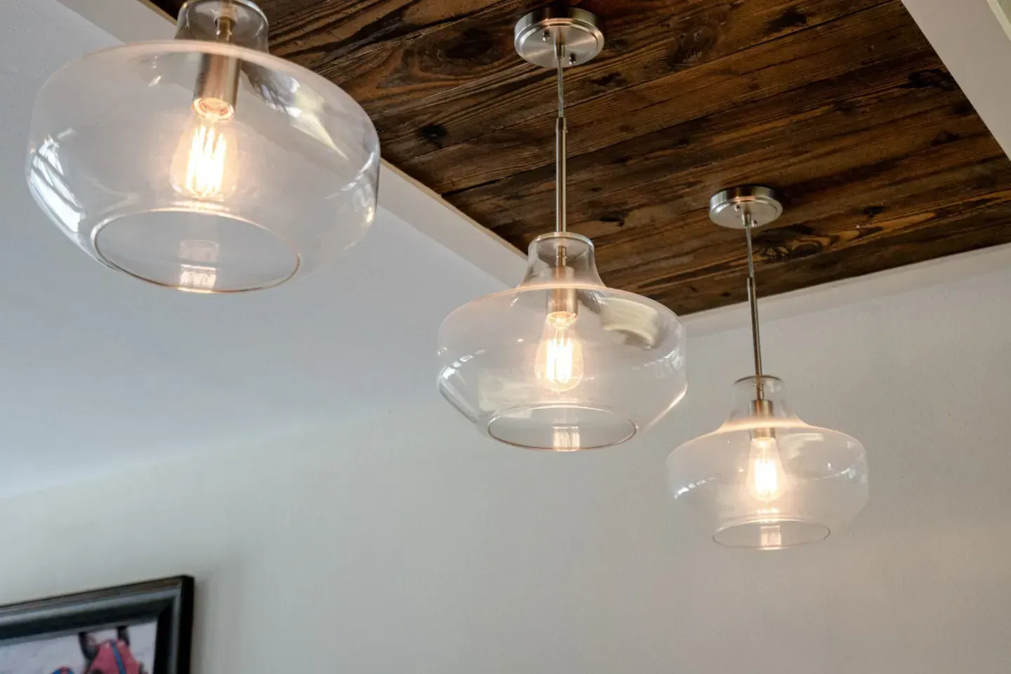 Three clear glass pendant lights are hanging from a wooden ceiling.
