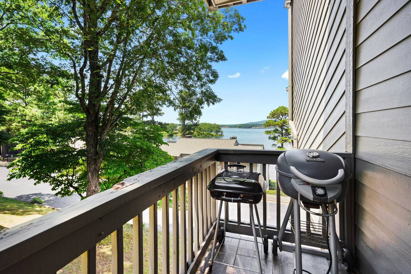 A balcony with a grill and stools overlooking a lake.