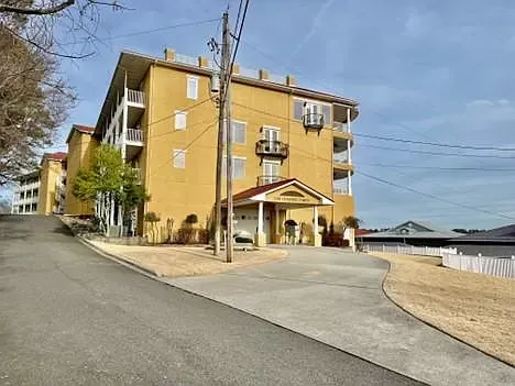 A large yellow building is sitting on top of a hill next to a road.