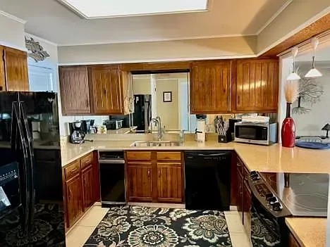 A kitchen with wooden cabinets , black appliances , a rug and a refrigerator.