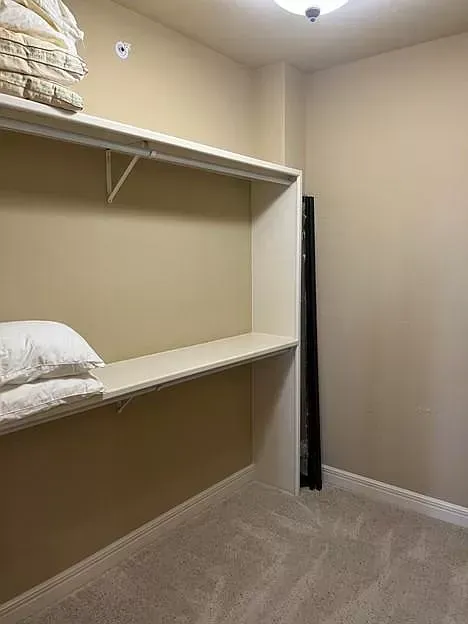 A walk in closet with a shelf and pillows on it.