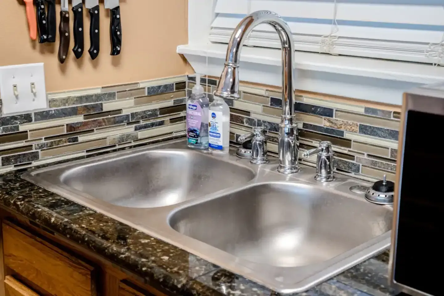 A kitchen sink with a soap dispenser and knives hanging on the wall.