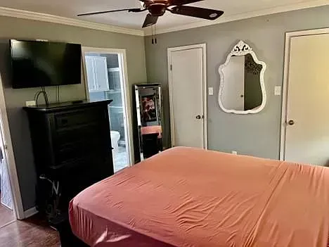 A bedroom with a bed , dresser , television , mirror and ceiling fan.