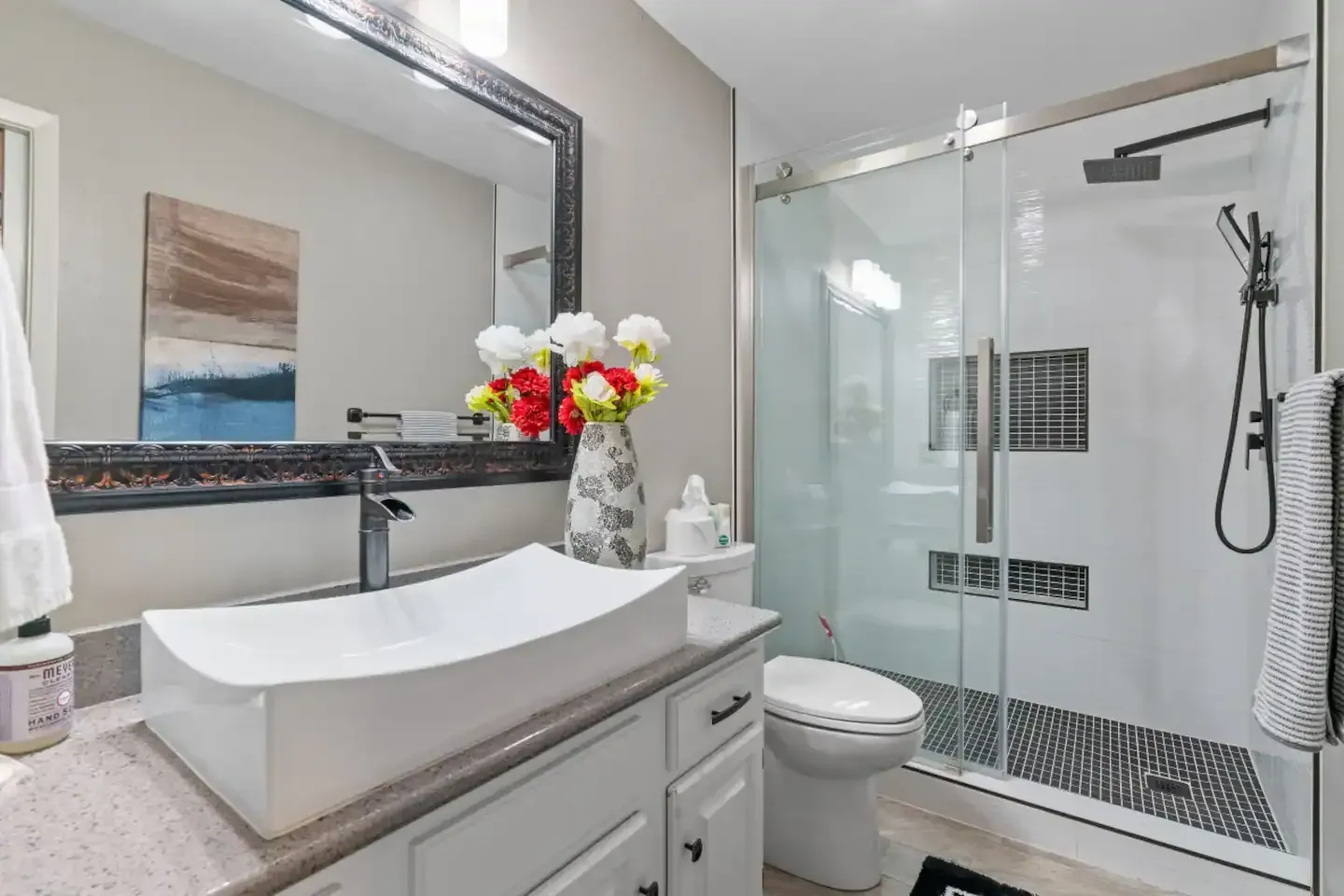 A bathroom with a sink , toilet , shower and mirror.