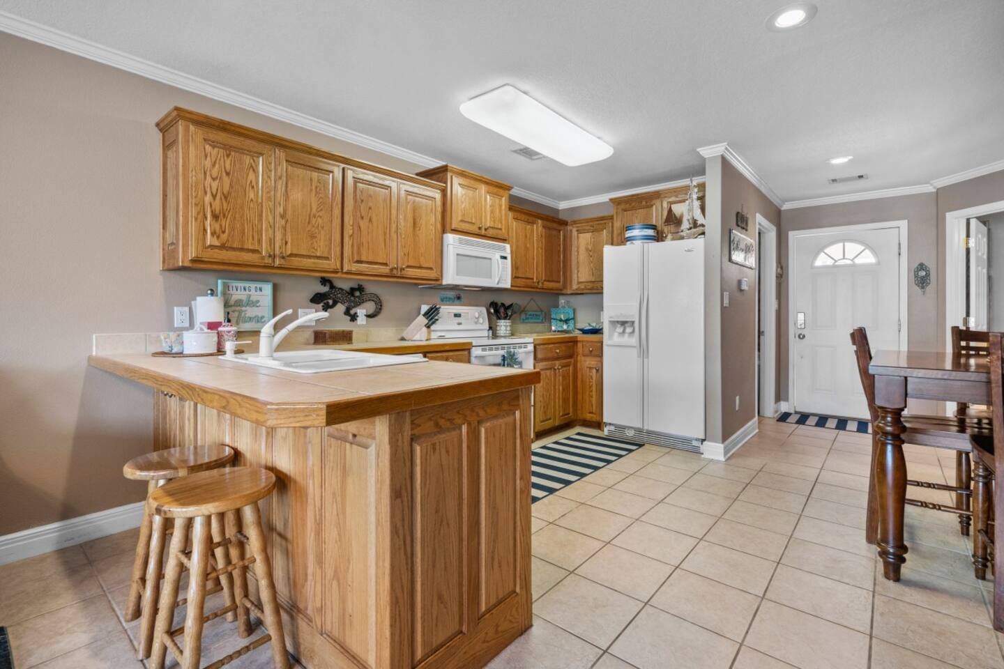 A kitchen with wooden cabinets , stools , a refrigerator and a table.