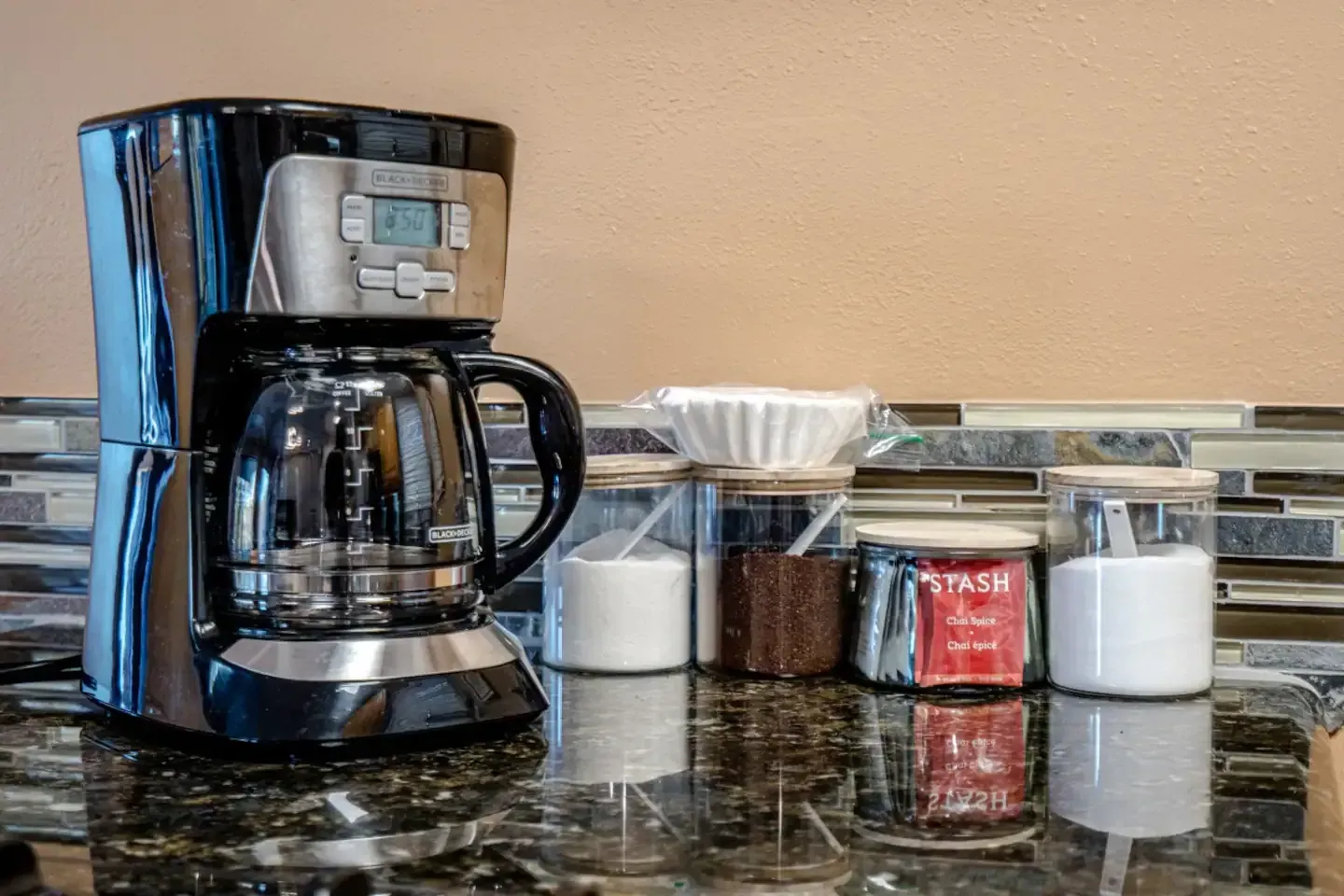 A coffee maker is sitting on a counter next to jars of sugar and salt.