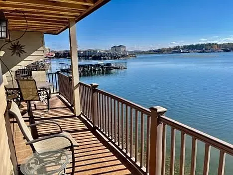 A balcony overlooking a lake with chairs and a table.