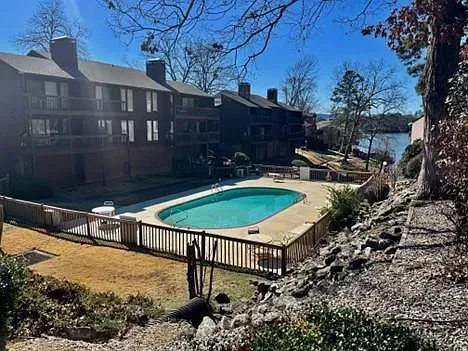 A large swimming pool is surrounded by a fence in front of a building.