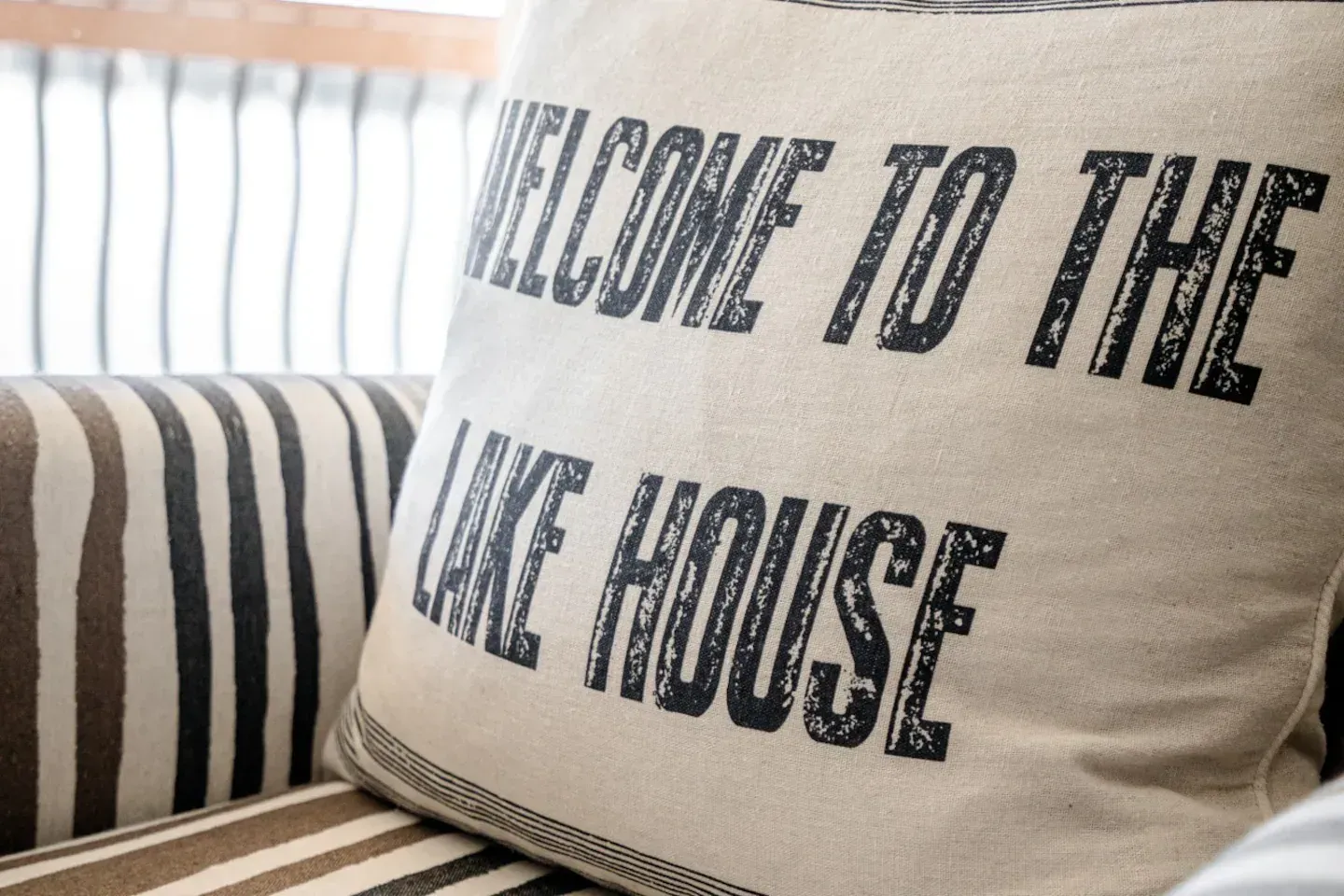 A pillow on a couch that says welcome to the lake house