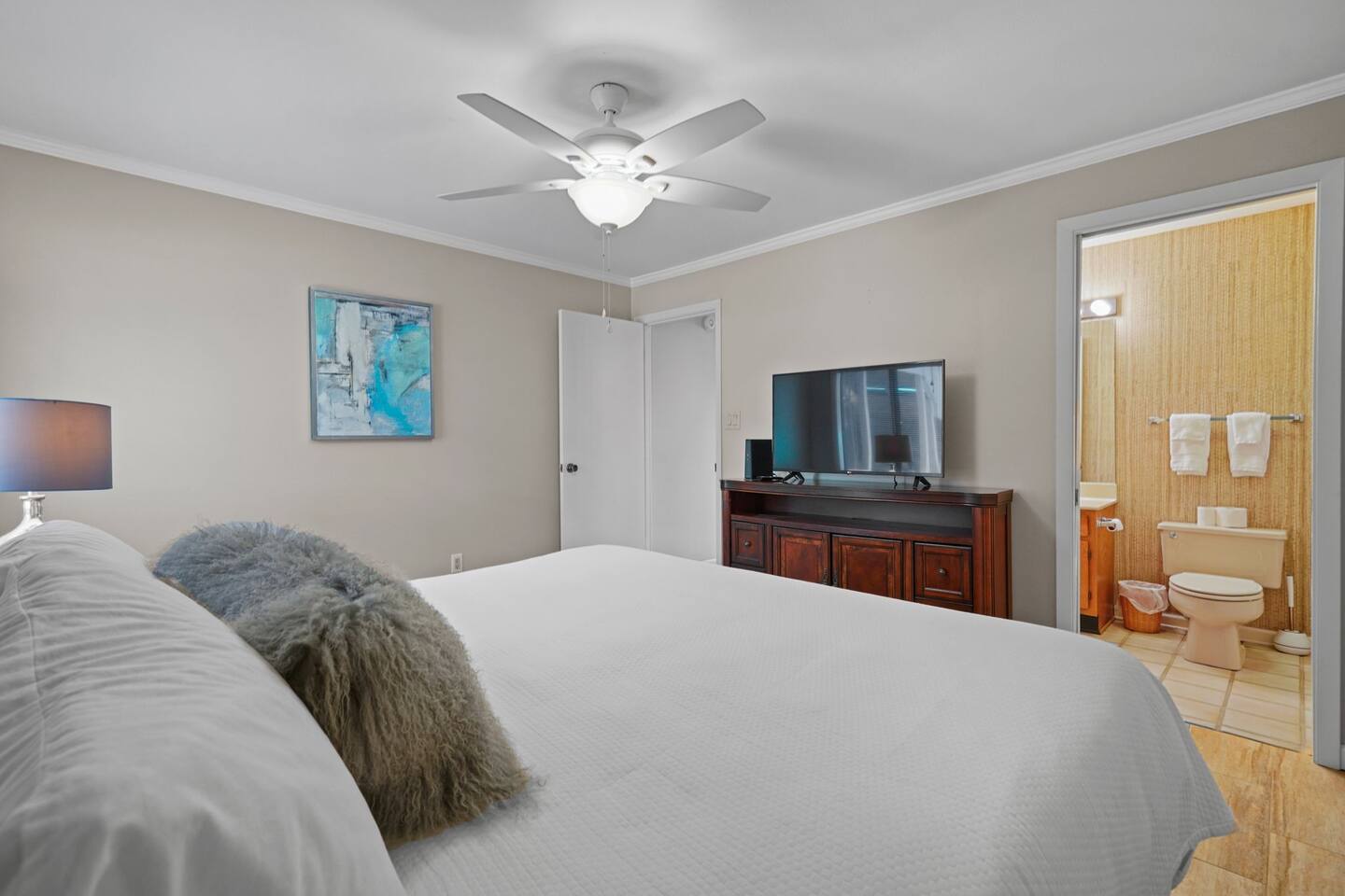 A bedroom with a king size bed , a television , a ceiling fan and a bathroom.