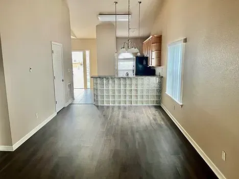 An empty living room with hardwood floors and a kitchen in the background.