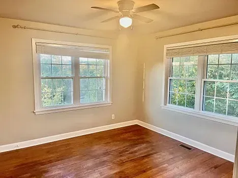Empty bedroom with hardwood floors, two windows with shades, and a ceiling fan.