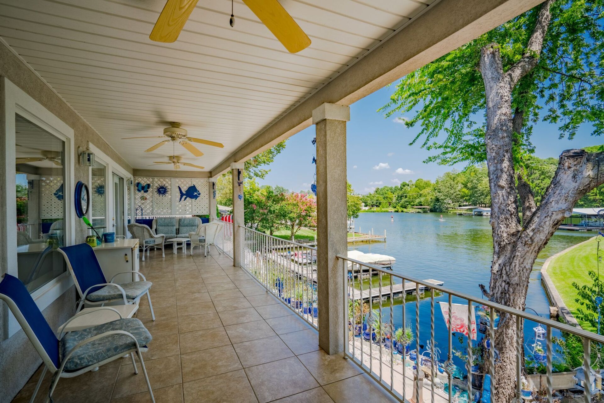 A large porch with chairs and a ceiling fan overlooking a lake.