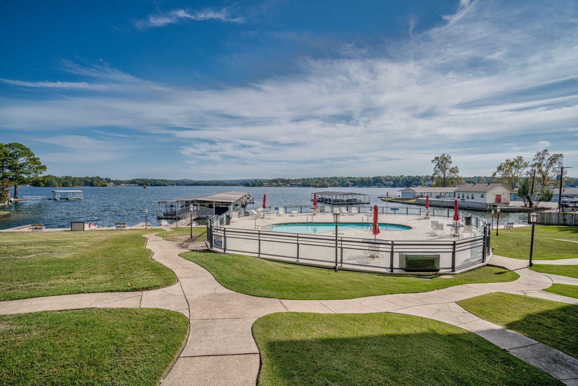 There is a swimming pool in the middle of a lush green field next to a lake.