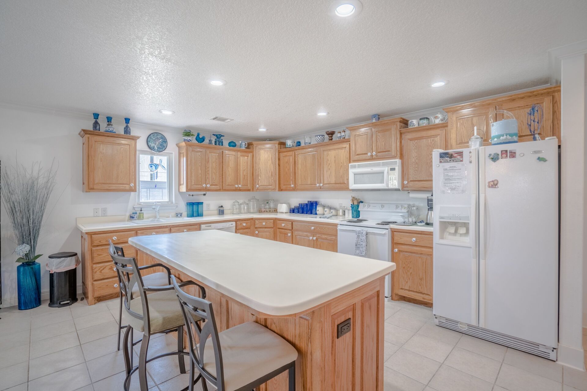 A kitchen with wooden cabinets , a large island , a refrigerator and a microwave.