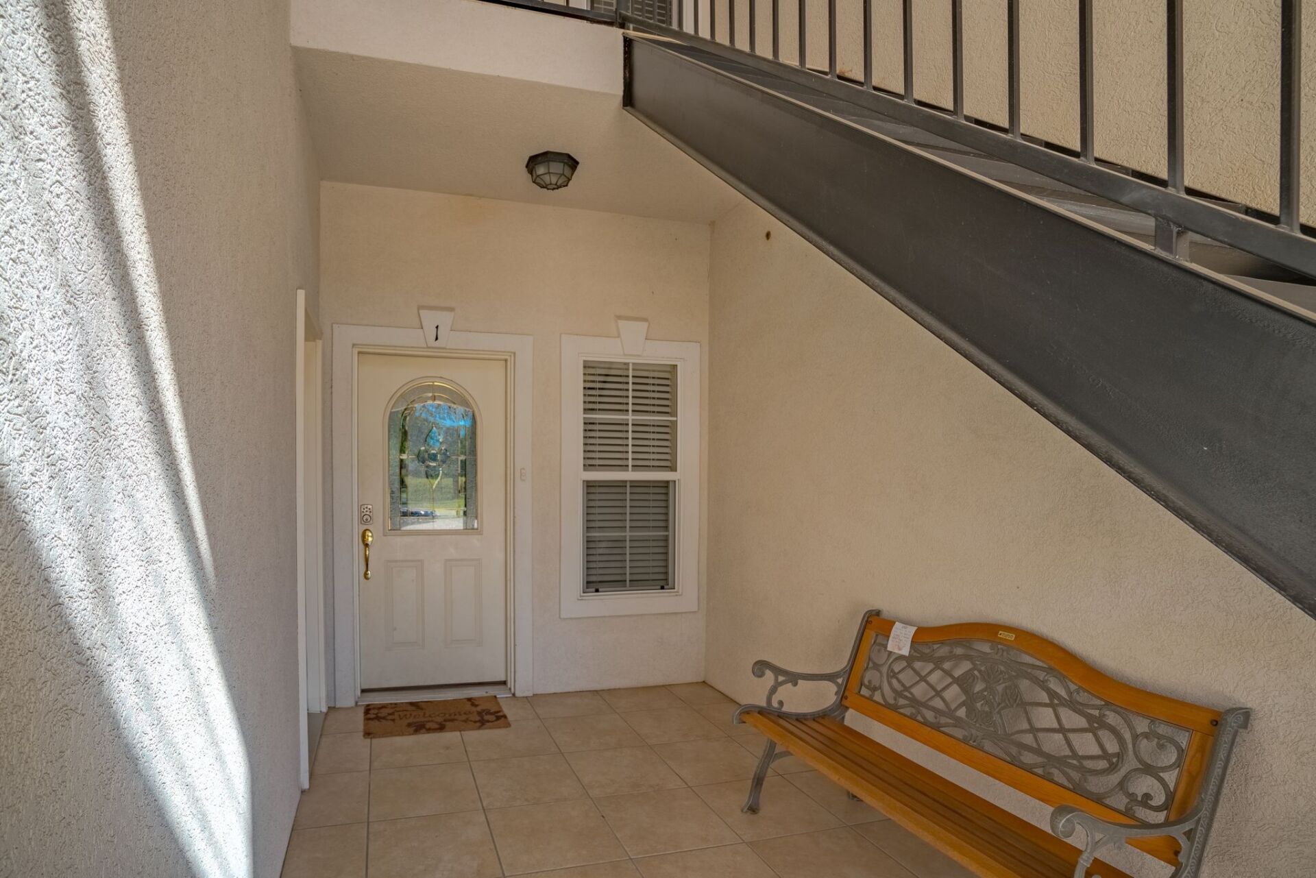 A hallway with stairs leading up to a door and a bench