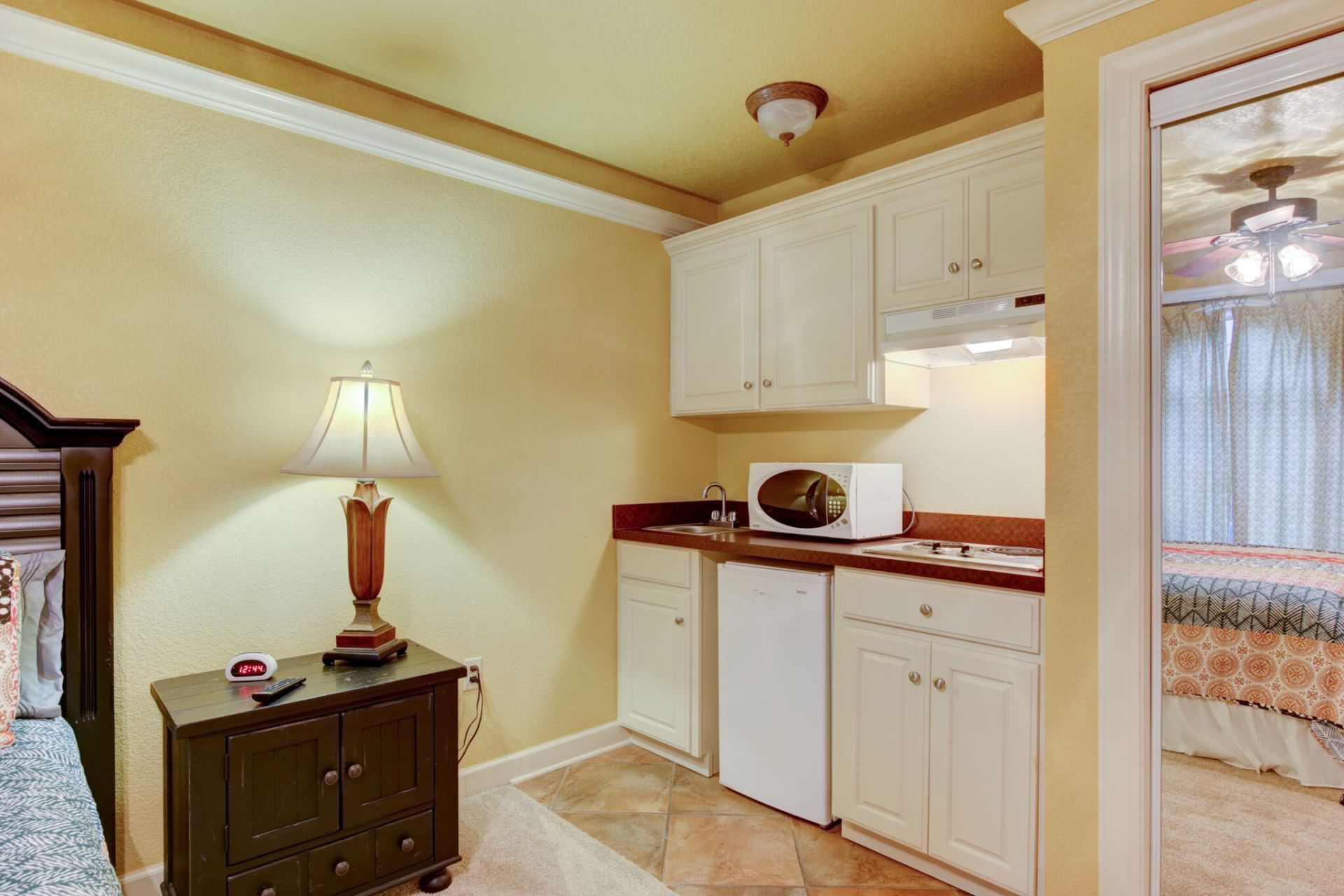 A small kitchen with a microwave , sink , cabinets and a lamp.