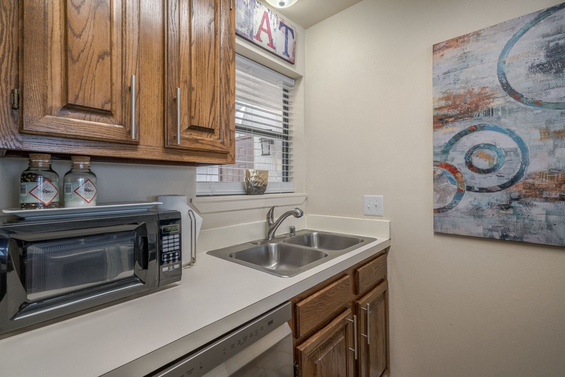 A kitchen with two sinks , a microwave , and a painting on the wall.