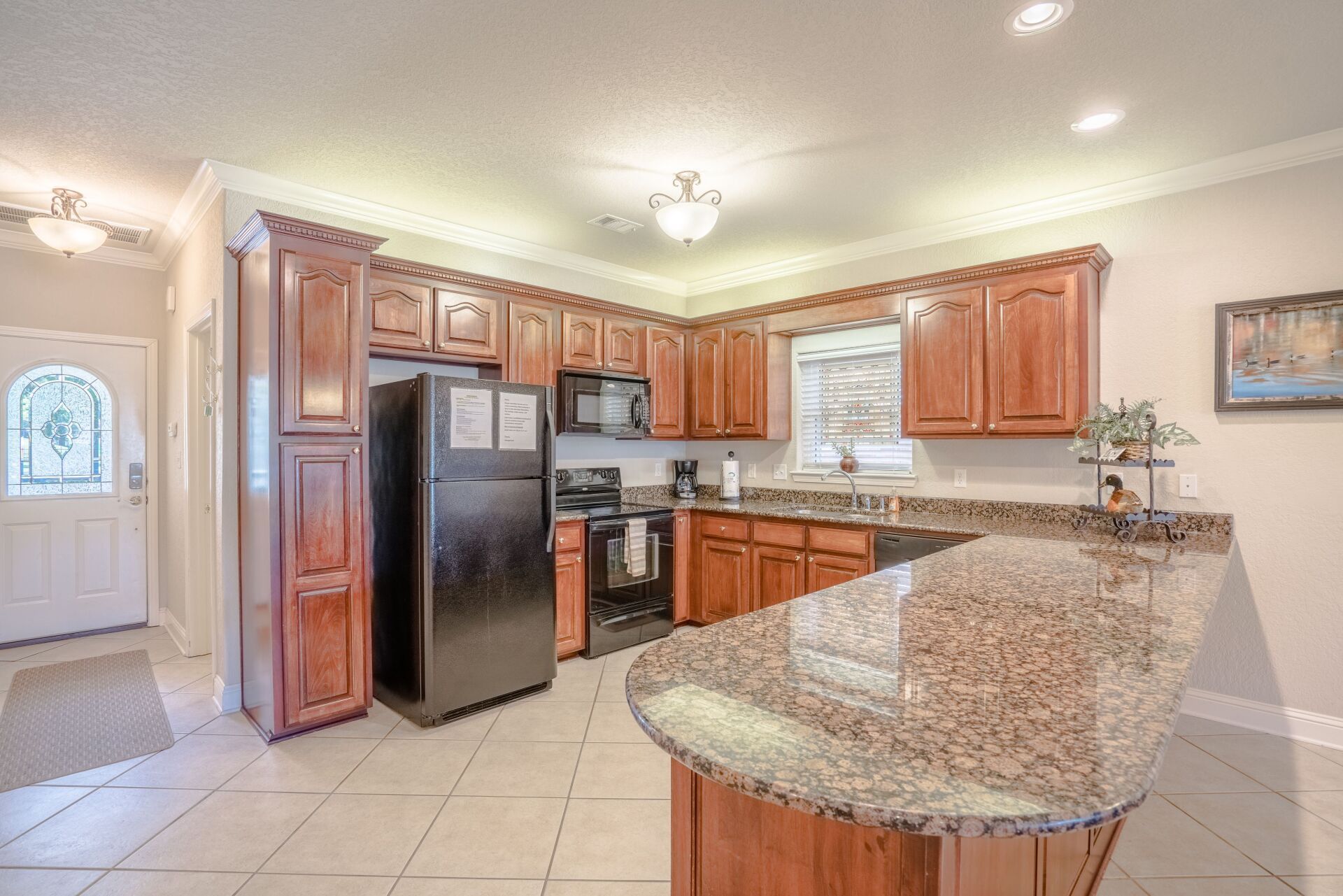 A kitchen with wooden cabinets , granite counter tops , a refrigerator , stove , microwave and sink.
