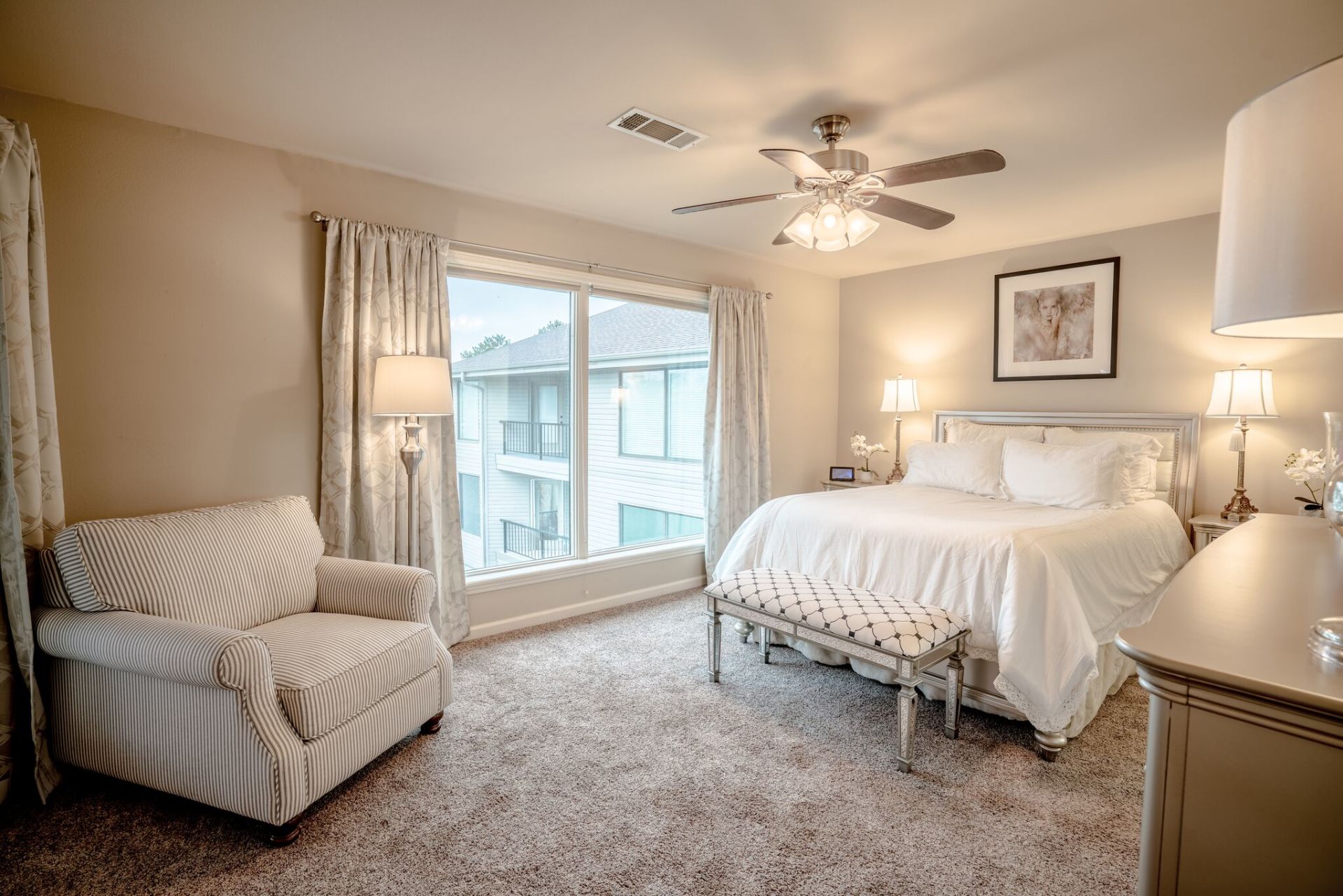 A bedroom with a bed , chair , dresser and ceiling fan.