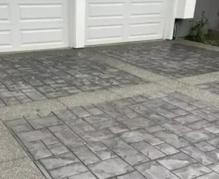 A brick walkway leading to a house next to a driveway.