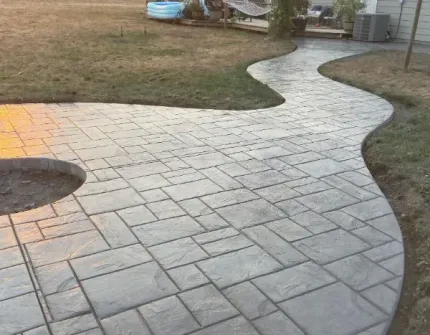 A concrete walkway leading to a fire pit in a backyard.