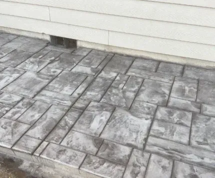 A gray brick walkway next to a white house.