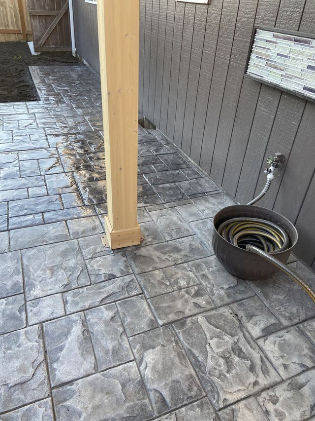 A hose is sitting on a concrete patio next to a wooden post.