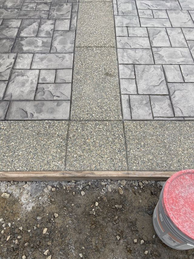 A bucket of concrete is sitting on the ground next to a brick walkway.