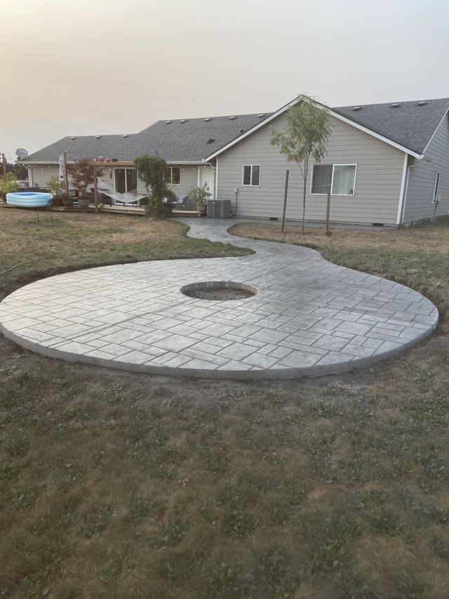 A concrete patio with a fire pit in the middle of it in front of a house.