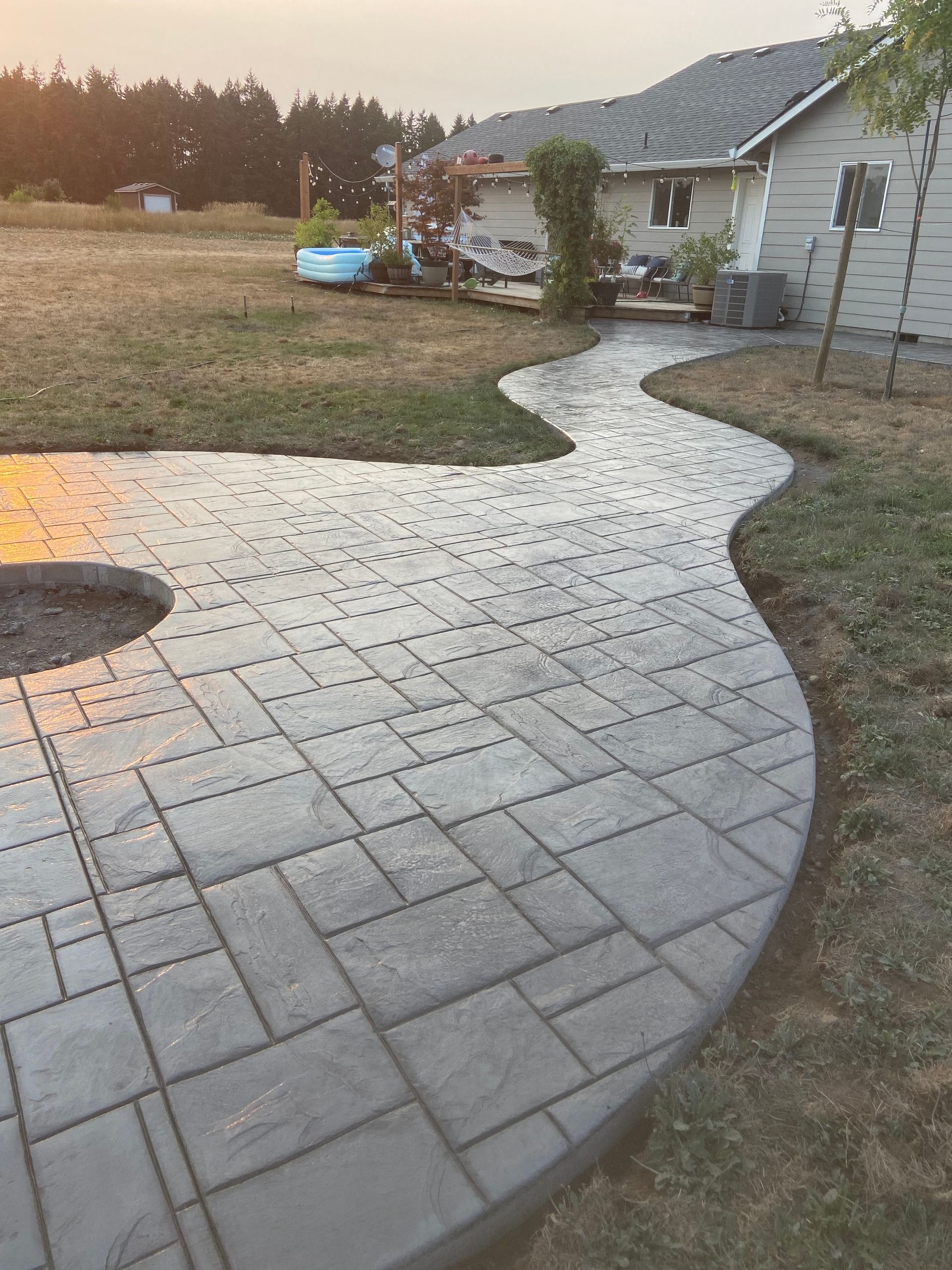 A patio with a fire pit in the middle of it and a house in the background.