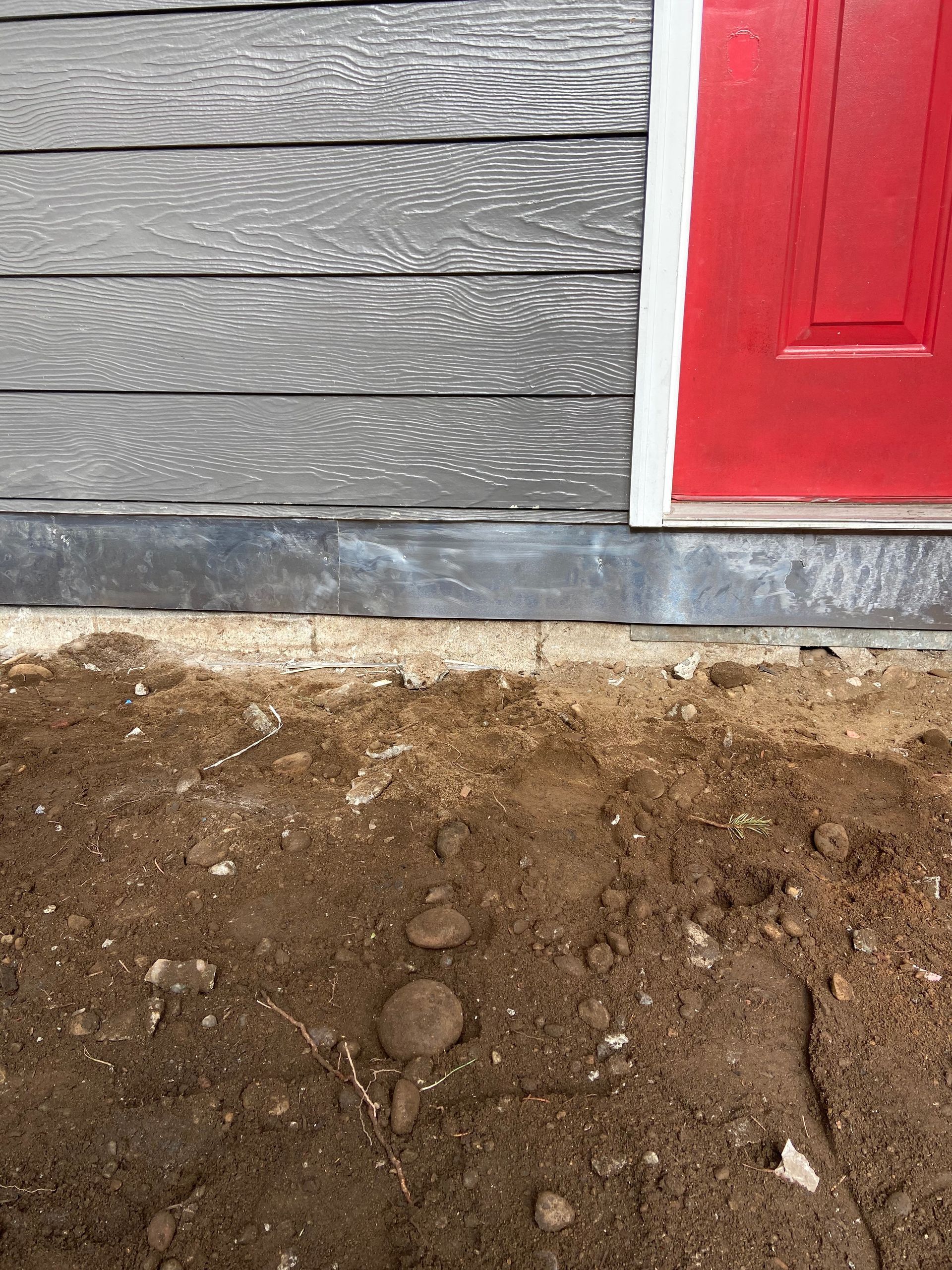A red door is on the side of a house next to a pile of dirt.