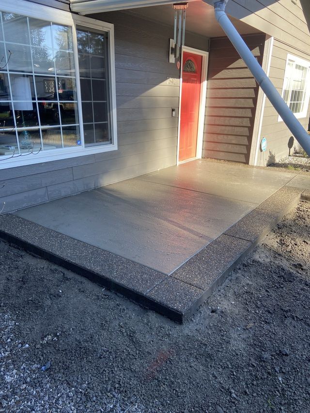 A concrete patio in front of a house with a red door.