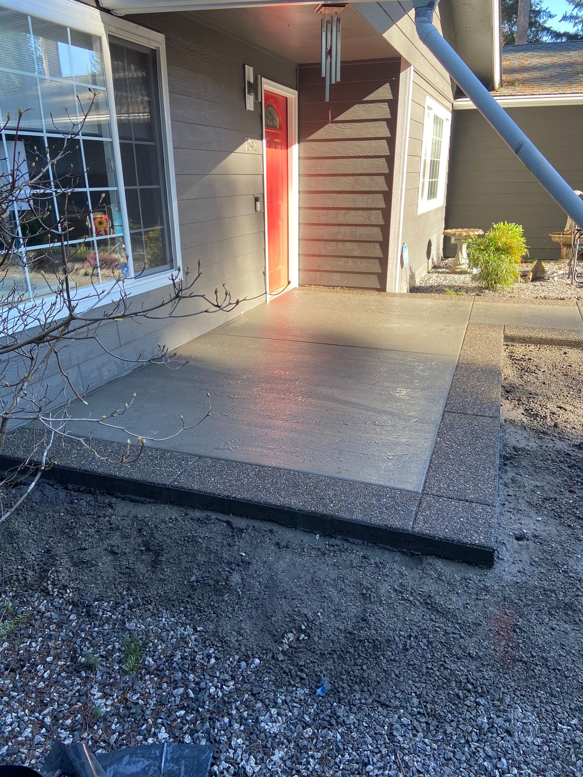 A concrete porch with a red door in front of a house.