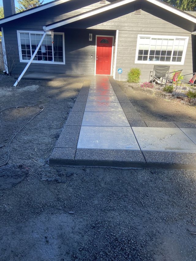 A concrete walkway leading to a house with a red door.