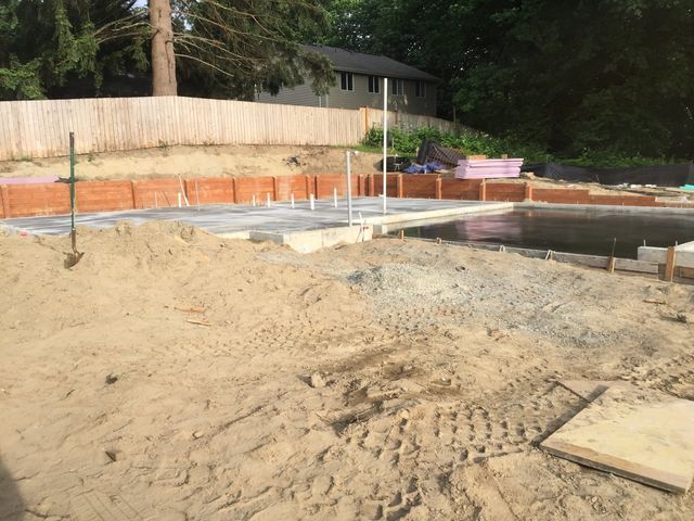 A large pile of sand is sitting in front of a house under construction.